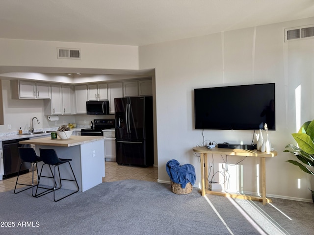 kitchen featuring a breakfast bar, black appliances, sink, gray cabinets, and light tile patterned floors