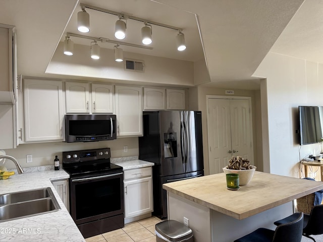 kitchen with appliances with stainless steel finishes, a kitchen breakfast bar, sink, light tile patterned floors, and white cabinets