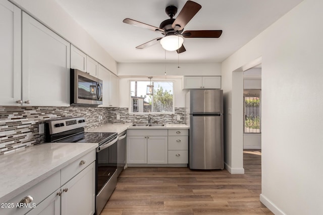 kitchen with light wood-style floors, appliances with stainless steel finishes, light countertops, backsplash, and a sink