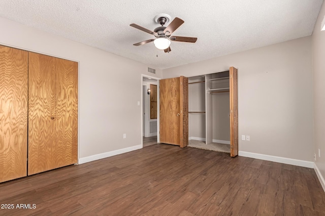 unfurnished bedroom with a textured ceiling, two closets, visible vents, baseboards, and wood finished floors