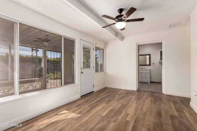 interior space with ceiling fan, visible vents, baseboards, a textured ceiling, and wood finished floors
