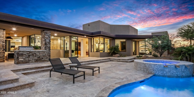 back of property at dusk with a patio area, a pool with connected hot tub, and exterior kitchen