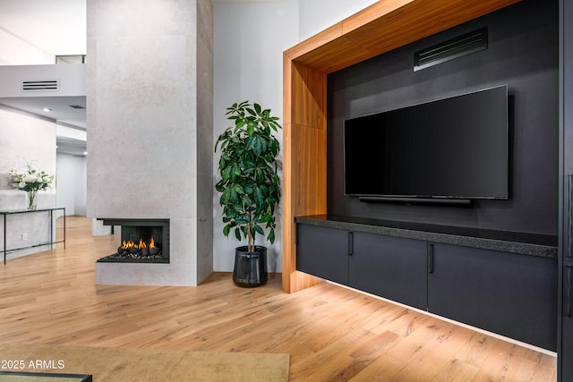 unfurnished living room with light wood-type flooring, visible vents, a fireplace, and a high ceiling