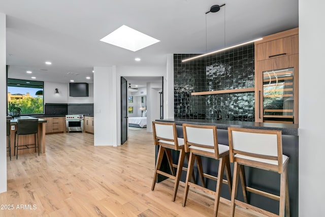 bar with light wood finished floors, beverage cooler, a skylight, high end range, and a sink