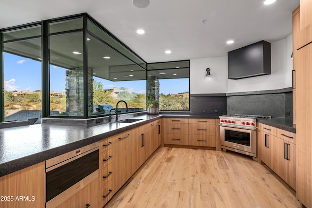 kitchen featuring a sink, a healthy amount of sunlight, light wood-style floors, luxury range, and wall chimney exhaust hood