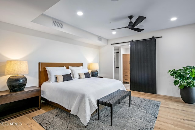 bedroom featuring a barn door, wood finished floors, visible vents, and recessed lighting