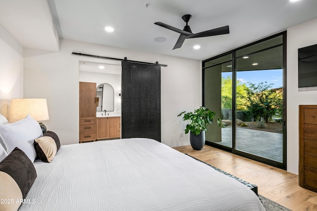 bedroom featuring a barn door, a sink, wood finished floors, a wall of windows, and access to outside