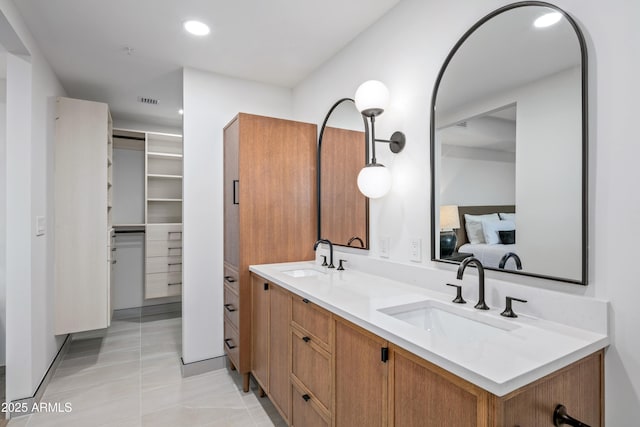 bathroom with double vanity, a sink, a walk in closet, and recessed lighting