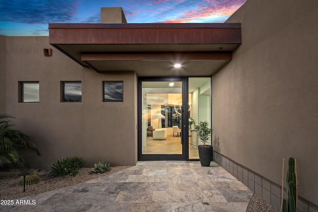 exterior entry at dusk featuring a patio and stucco siding