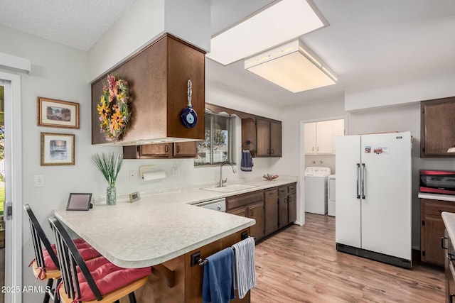 kitchen featuring sink, a kitchen bar, white refrigerator, washing machine and clothes dryer, and kitchen peninsula