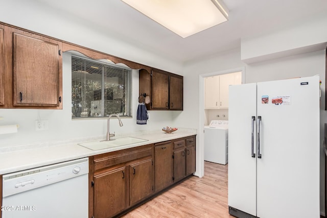 kitchen with white appliances, washer / clothes dryer, sink, and light hardwood / wood-style flooring