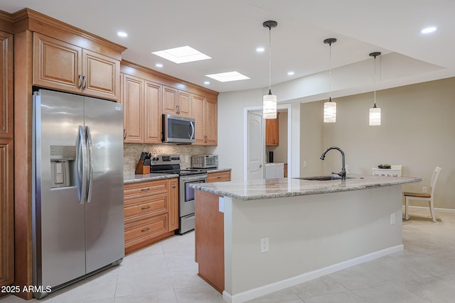 kitchen with light stone counters, decorative light fixtures, stainless steel appliances, an island with sink, and sink