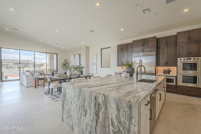 kitchen with light stone counters, vaulted ceiling, visible vents, a sink, and appliances with stainless steel finishes