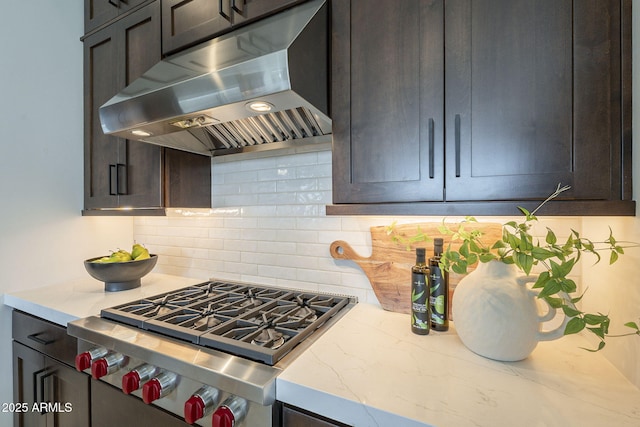 kitchen featuring tasteful backsplash, dark brown cabinets, light stone counters, stovetop, and under cabinet range hood