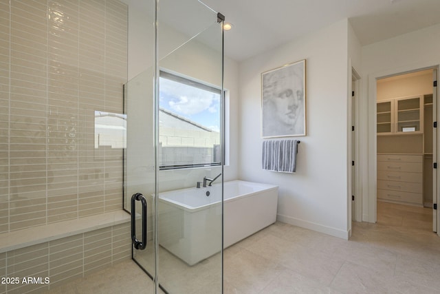 full bath featuring a shower stall, a spacious closet, tile patterned floors, baseboards, and a freestanding tub