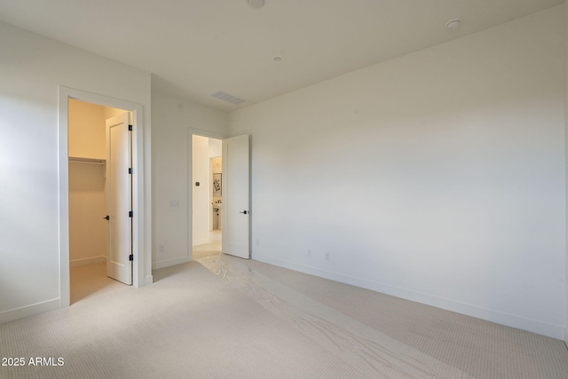 unfurnished bedroom with a spacious closet, visible vents, light carpet, a closet, and baseboards