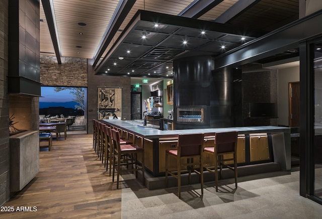 bar featuring wood finished floors, beamed ceiling, and a fireplace