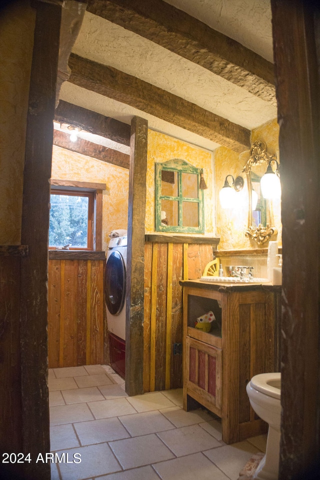 bathroom with washer / clothes dryer, toilet, wood walls, lofted ceiling with beams, and tile patterned floors