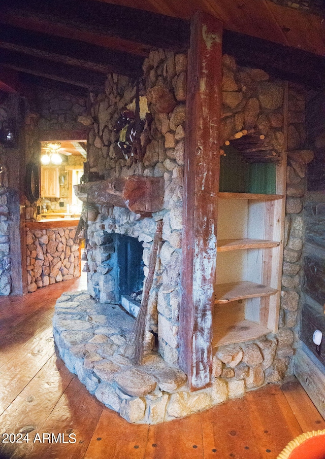 unfurnished living room with beam ceiling, a stone fireplace, and hardwood / wood-style flooring