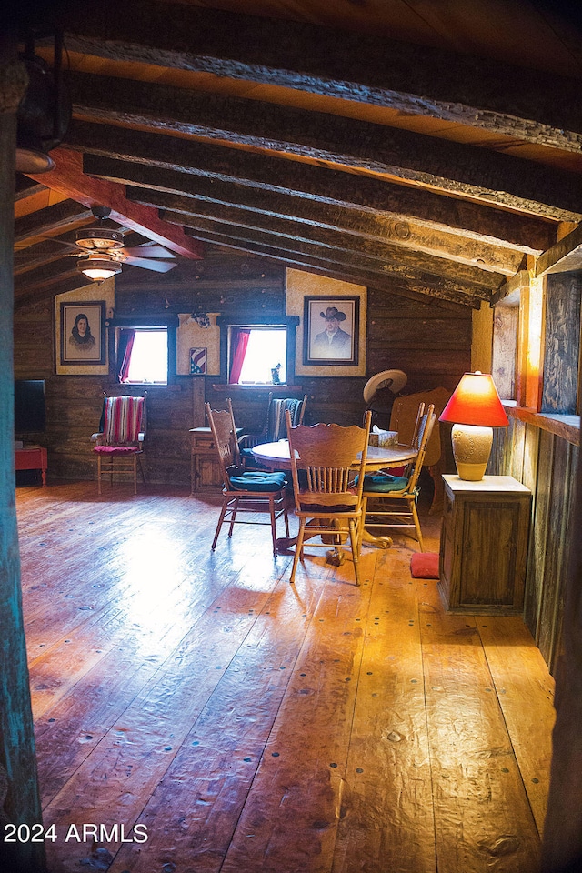 dining room featuring vaulted ceiling with beams, hardwood / wood-style floors, wooden walls, and ceiling fan