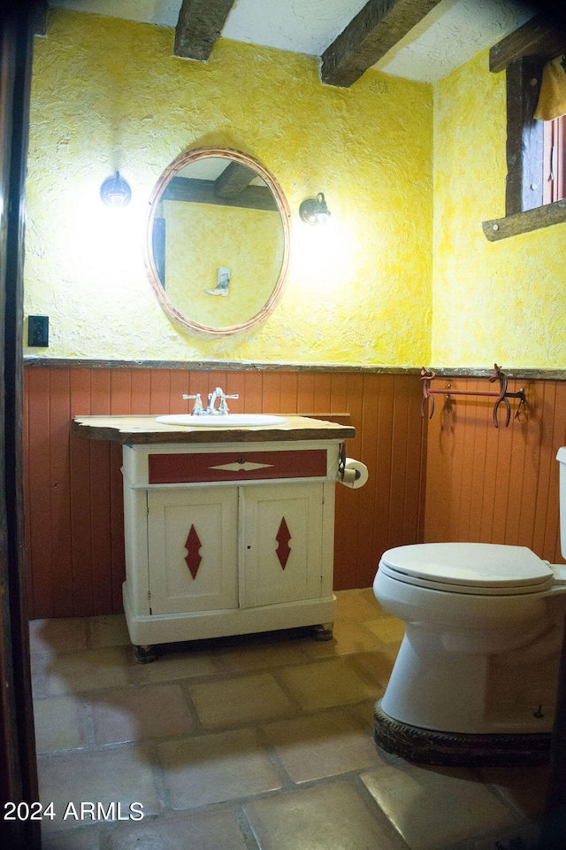 bathroom with beam ceiling, vanity, toilet, and wood walls