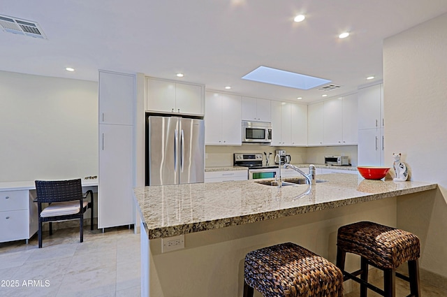 kitchen featuring visible vents, appliances with stainless steel finishes, a peninsula, light stone countertops, and a sink