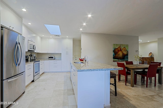 kitchen with a kitchen island with sink, a breakfast bar, a sink, white cabinets, and appliances with stainless steel finishes