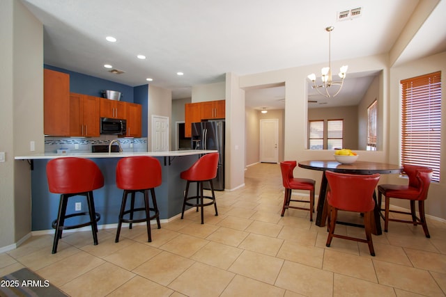 kitchen with black microwave, stainless steel refrigerator with ice dispenser, a chandelier, a peninsula, and light countertops