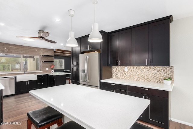 kitchen with a sink, light countertops, appliances with stainless steel finishes, hanging light fixtures, and a center island