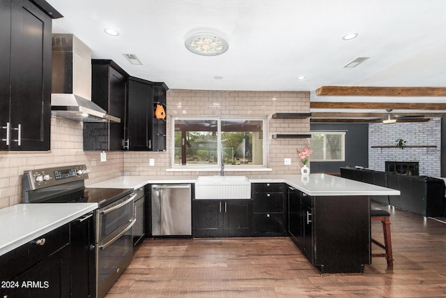 kitchen featuring appliances with stainless steel finishes, open floor plan, light countertops, wall chimney range hood, and a sink