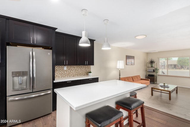 kitchen with open floor plan, light countertops, stainless steel refrigerator with ice dispenser, a kitchen bar, and decorative light fixtures