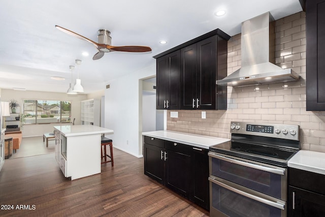 kitchen featuring a breakfast bar area, light countertops, hanging light fixtures, wall chimney range hood, and double oven range