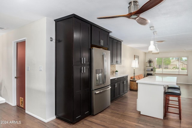 kitchen with dark cabinets, a kitchen island, light countertops, stainless steel fridge with ice dispenser, and pendant lighting