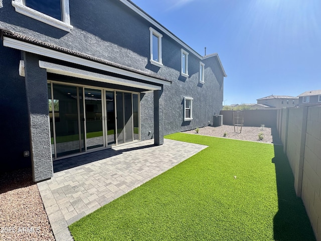 back of property with central AC unit, stucco siding, a lawn, a fenced backyard, and a patio area