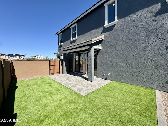 rear view of house with stucco siding, a patio, a lawn, and a fenced backyard