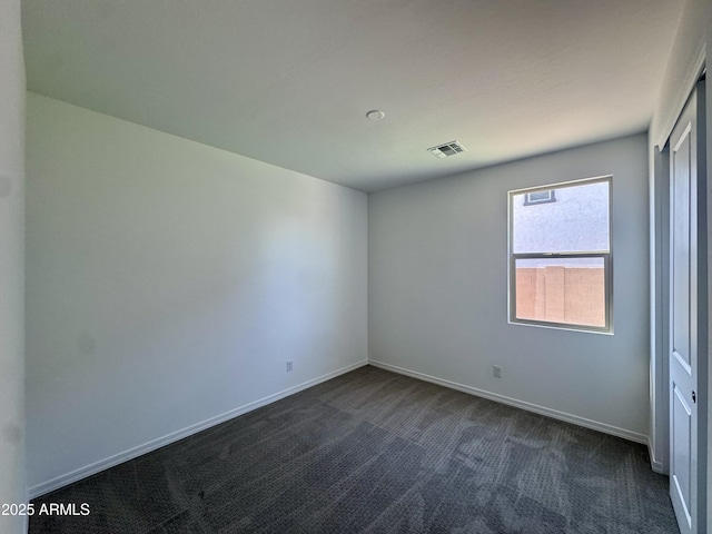 spare room featuring visible vents, baseboards, and dark carpet