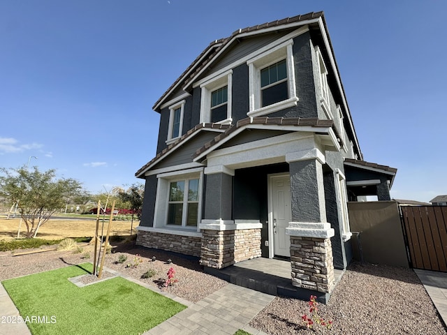 view of front of property featuring stucco siding, stone siding, and a gate