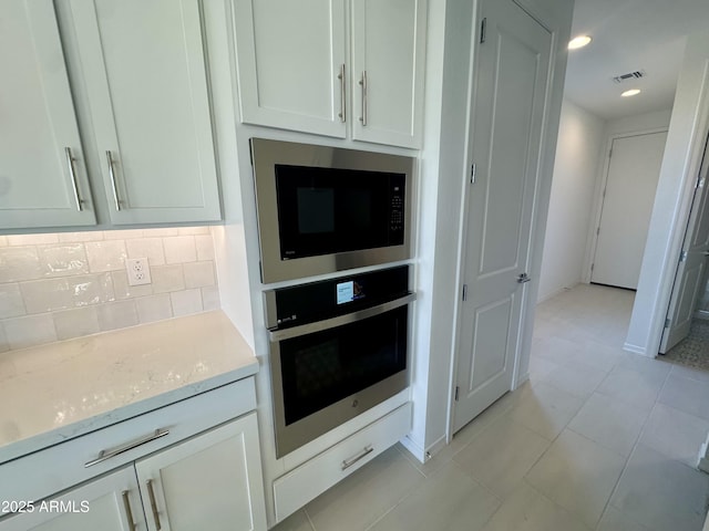 kitchen with oven, visible vents, light stone counters, backsplash, and black microwave