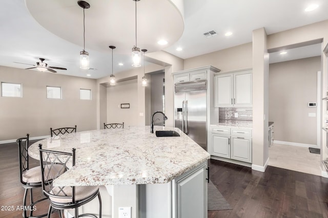 kitchen with built in fridge, sink, white cabinets, and a spacious island