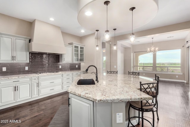 kitchen with premium range hood, sink, a breakfast bar area, white cabinetry, and a large island