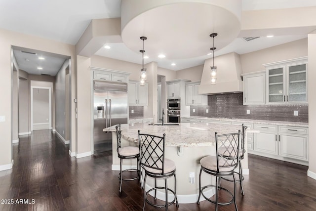 kitchen with white cabinetry, decorative light fixtures, custom range hood, and appliances with stainless steel finishes