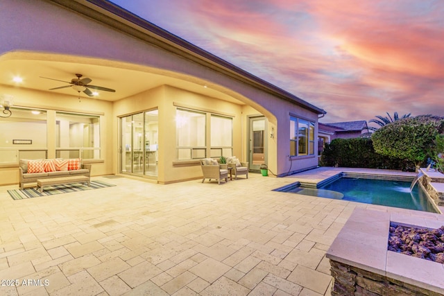 pool at dusk with a patio, pool water feature, and ceiling fan