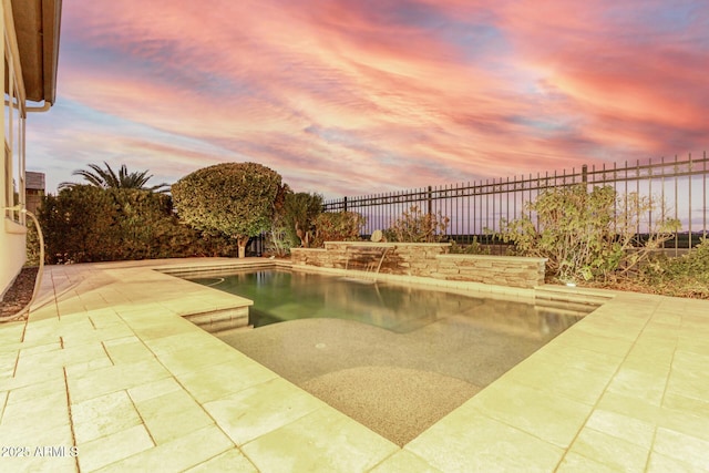 pool at dusk featuring pool water feature and a patio