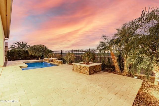 pool at dusk featuring pool water feature, a patio area, and a fire pit