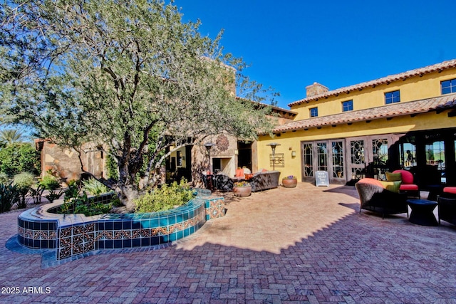 rear view of house with a patio area, french doors, and an outdoor stone fireplace