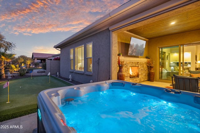 pool at dusk with a hot tub and an outdoor stone fireplace