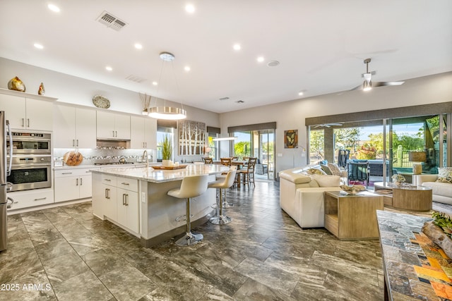 kitchen featuring white cabinetry, decorative light fixtures, a kitchen island with sink, and tasteful backsplash