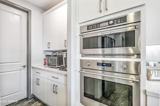 kitchen with dark wood-type flooring, stainless steel double oven, tasteful backsplash, and white cabinets