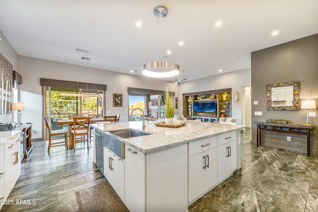 kitchen with sink, white cabinetry, hanging light fixtures, an island with sink, and light stone countertops