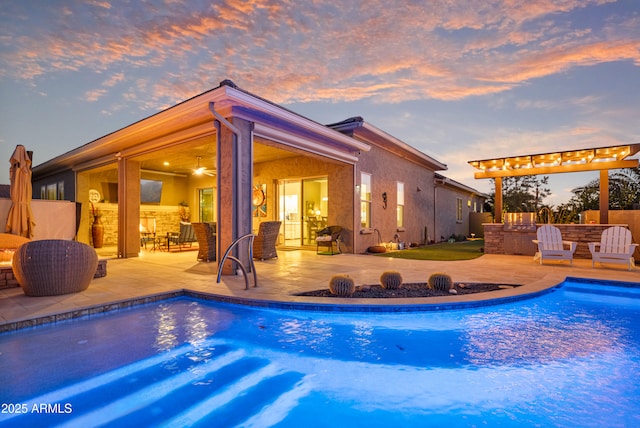 pool at dusk featuring an outdoor kitchen, ceiling fan, and a patio